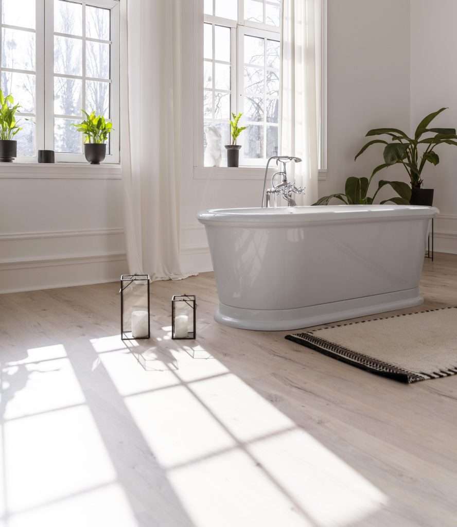 Luxe lichte badkamer met vrijstaand bad, grote ramen, houten vloer en veel groene planten voor een moderne wellness uitstraling.