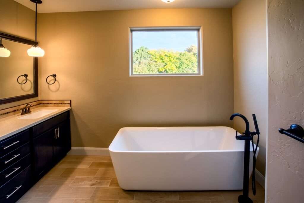 Moderne badkamer met vrijstaand bad, houten vloertegels, zwart badkraan, grote spiegel en natuurlijk licht – inspiratie voor luxe badkamer, minimalistisch design, strakke uitstraling.