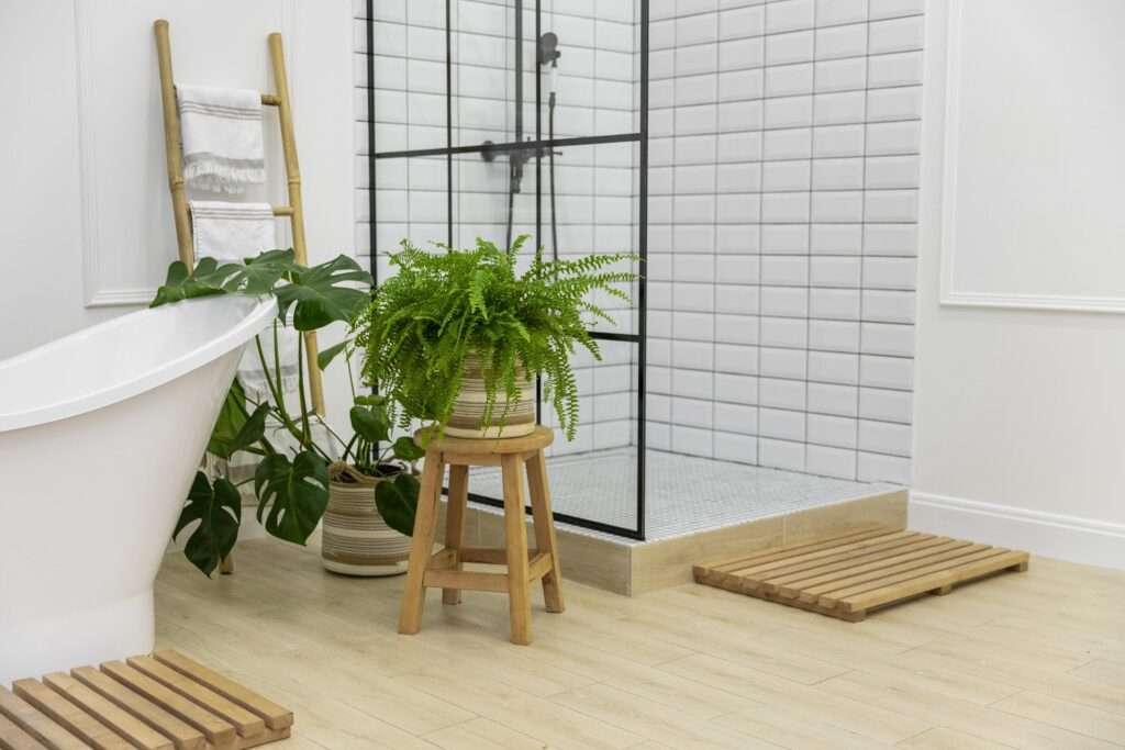 Scandinavische badkamer met witte tegels, moderne inloopdouche, vrijstaand bad, houten accenten en groene kamerplanten – duurzame en natuurlijke badkamerinspiratie.