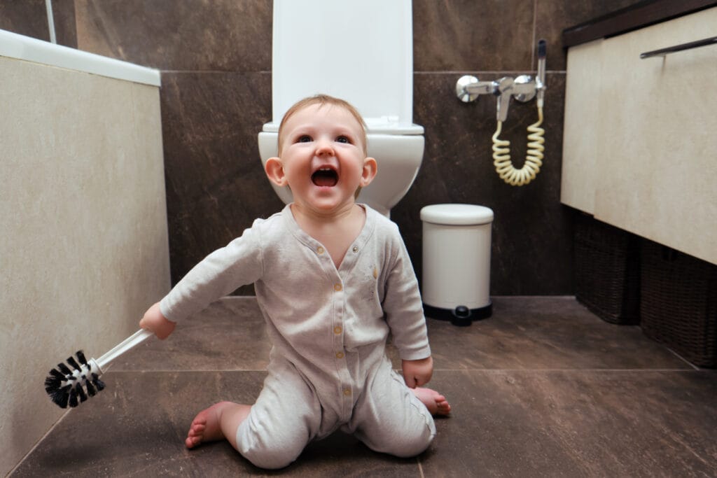 Lachende baby op bruine vloertegels in een moderne toiletruimte met grote wandtegels en wit sanitair, ideaal voor inspiratie voor kindvriendelijke toiletinrichting met tegels.