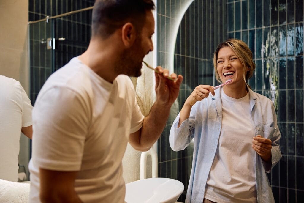 Twee mensen poetsen hun tanden in een moderne badkamer met glanzende donkergroene wandtegels – inspiratie voor een eigentijdse, stijlvolle badkamer met keramische tegels.
