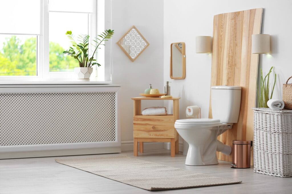 Lichte, moderne toiletruimte met grijze houtlook vloertegels, een witte toiletpot, houten accenten en planten voor het raam.