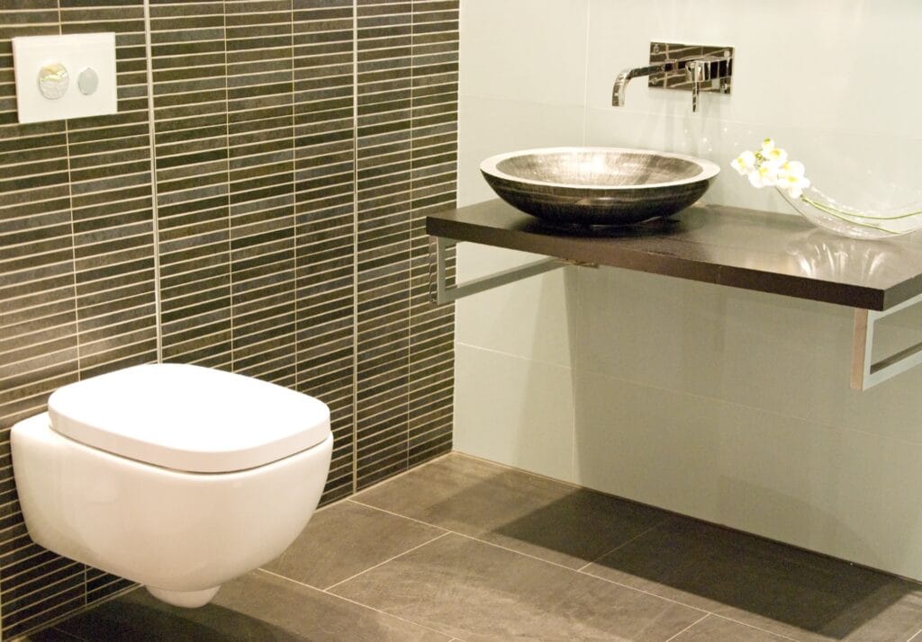 Stijlvolle moderne badkamer met donkere wandtegels, vrijhangend toilet en design waskom op een zwevend houten blad. Ideaal voor inspiratie voor luxe badkamer betegeling en moderne toiletruimte.