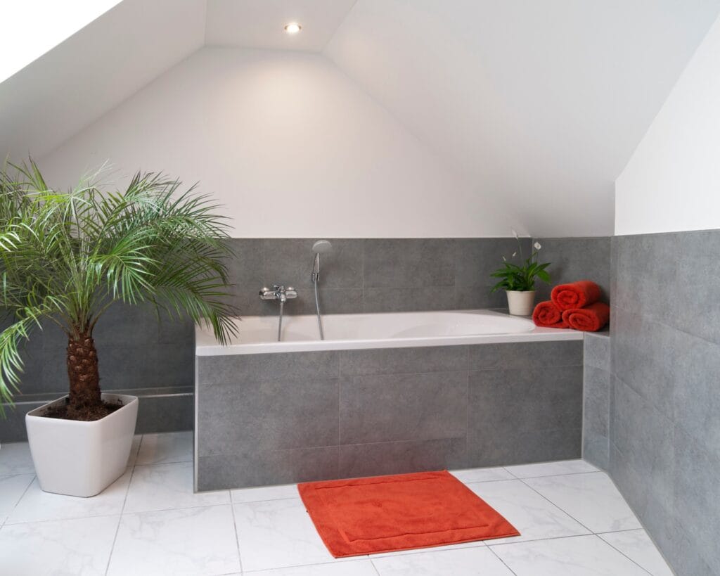 Badkamer op zolder met moderne grijze wandtegels en wit marmeren vloertegels, ligbad en groene planten. Ideaal voor inspiratie in badkamer betegelen.